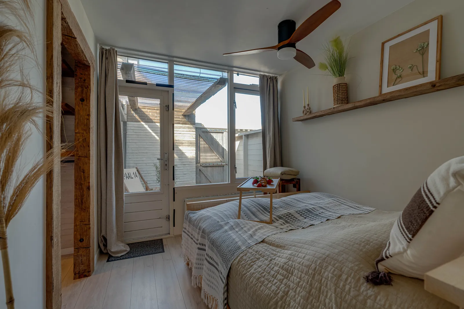 Slaapkamer met houten balken, plafondventilator en een deur naar de tuin