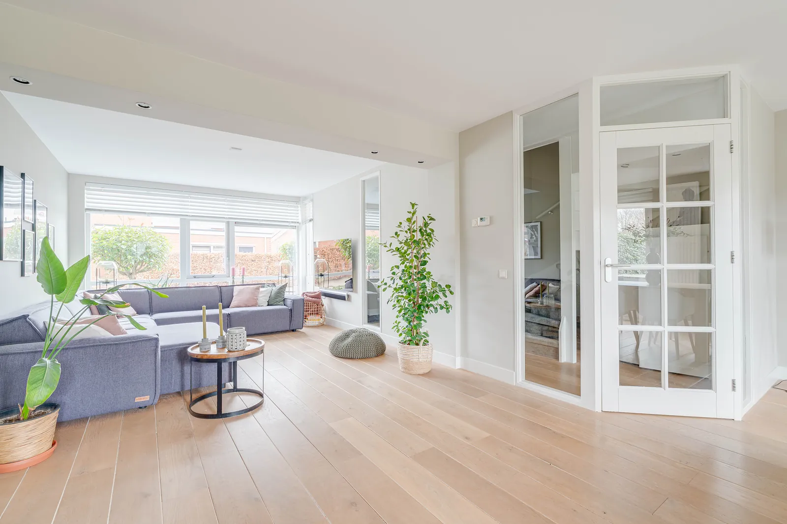 Ruime, lichte woonkamer met houten vloer, hoekbank en glazen deuren naar de hal