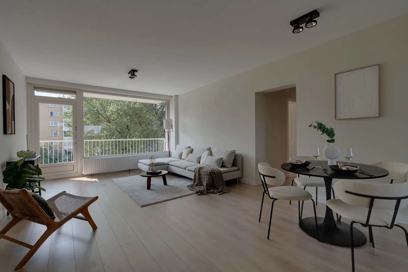 Woonkamer met lichte bank, ronde eettafel en een balkon met glazen schuifpui